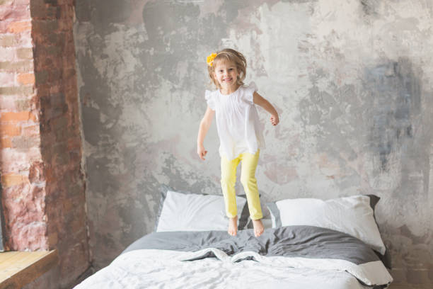 istock Happy child girl having fun jumping on a bed 1150695710