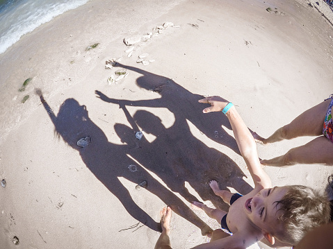 Family is having great time on the beach. There are their happy shadows on the sand. They raised their hands in the air.