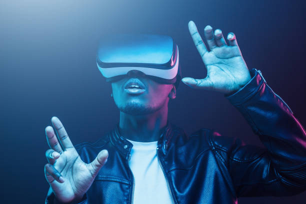 istock Young african man wearing virtual reality goggles with hands up, isolated on black background 1150698628