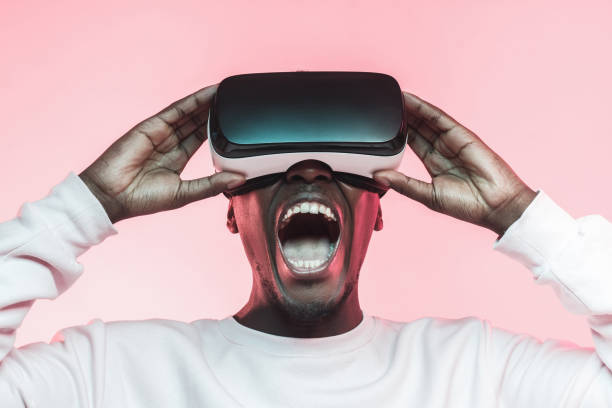 istock Young screaming african man experiencing virtual reality with VR headset, isolated on pink background 1150698644