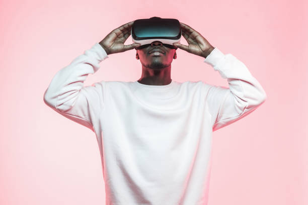 istock Young african man holding virtual reality goggles with both hands, isolated on pink background 1150698647