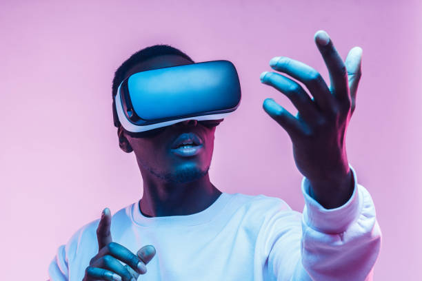 istock Young african american man playing game using VR glasses, enjoying 360 degree virtual reality headset for gaming, isolated on pink background 1150698673