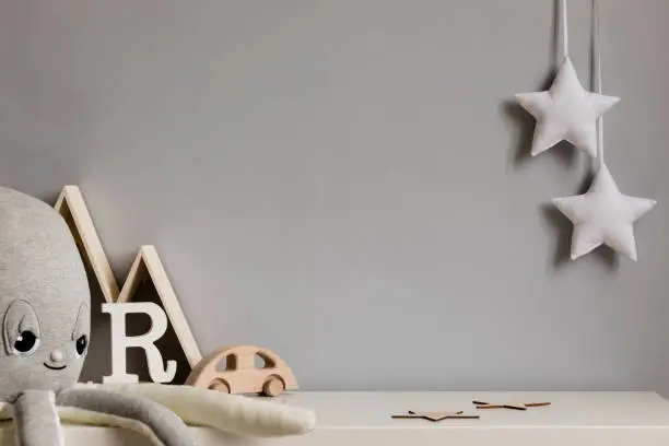 Photo of Stylish and cozy childroom with plush octopus, wooden mountain box, car and hanging white stars on the gray wall. Bright and sunny interior. Copy space. Minimalistic childish decor. Template.