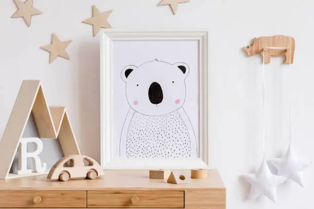 Photo of Stylish scandi childroom with white mock up photo frame, wooden accessories, toys, mountain box and stars pattern on the background wall. Bright and sunny interior. Template, Real photo. Wooden desk.