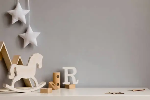 Photo of Stylish and cozy childroom with wooden mountain box, horse, blocks and hanging white stars on the gray wall. Bright and sunny interior. Copy space. Minimalistic childish decor. Template.