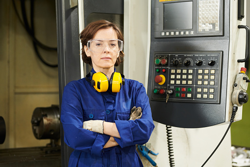 Waist up portrait of confident female worker posing by machine units in plant workshop, copy space