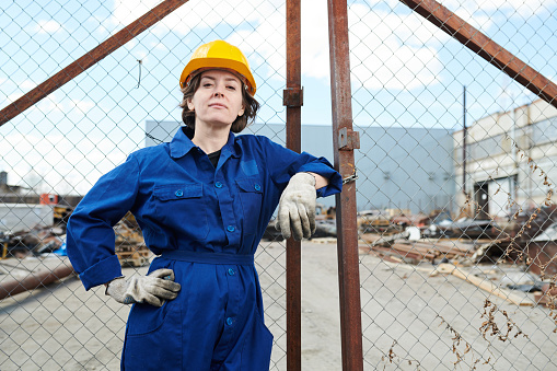 Portrait of empowered female worker posing against gates of construction site, copy space