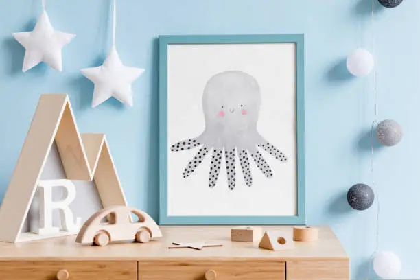 Photo of The modern scandinavian newborn baby room with mock up poster frame, wooden toys, mountain box and children accessories. Minimalistic and cozy interior with blue walls. Haniging cotton balls and stars