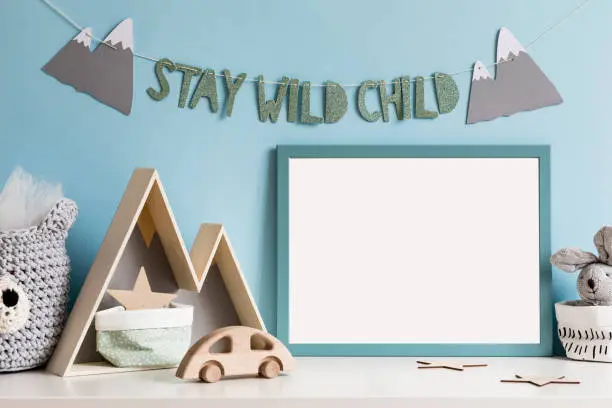 Photo of The modern scandinavian newborn baby room with mock up poster frame, wooden toys, mountain box and cotton basket with children accessories. Cozy interior with blue walls. Haniging stylish inscription