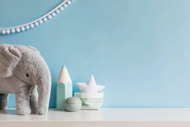 Photo of Cozy scandinavian newborn baby room with gray plush elephant ,white stars lamp and children accessories. Stylish interior with blue walls and haniging white garland. Template. Copy space.