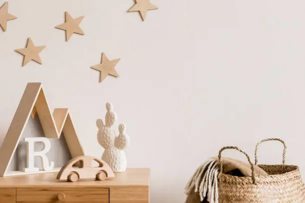 Photo of Stylish and cozy childroom with wooden accessories, toys, mountain box, car, basket and stars pattern on the background wall. Bright and sunny interior. Template, Real photo.