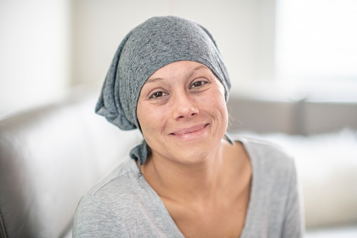 A beautiful woman with cancer sits in her hospital bed at home. She is looking into the camera in this portrait.