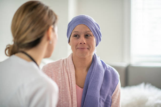 Doctor with a patient A young woman is indoors in a hospital. She has cancer, and her head is covered with a scarf. She is sitting next to her female doctor. cancer cell stock pictures, royalty-free photos & images