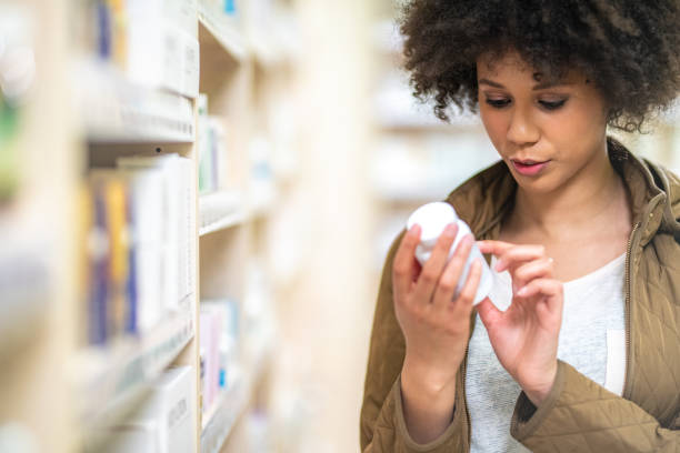 mujer leyendo etiqueta de la botella de medicina - pill bottle pharmacy medicine shelf fotografías e imágenes de stock