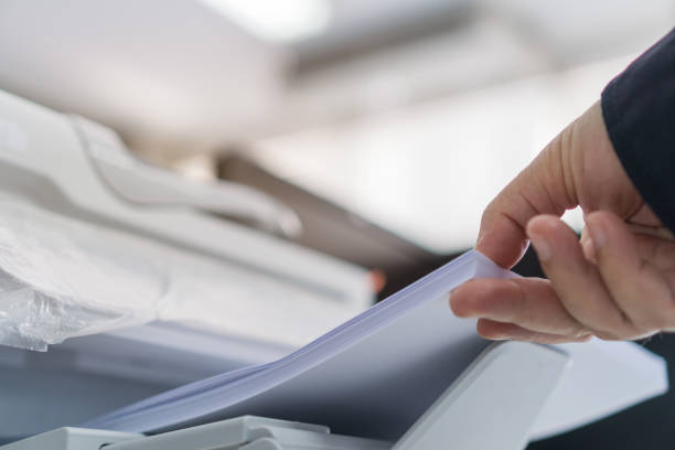 stampante aziendale / documenti di stampa nel concetto di ufficio: l'uomo d'affari preme carta bianca in alimentatore di cartucce stampato al laser, macchina scanner per copiare documento per segnalare in uffici moderni affollati sfondo - copy area foto e immagini stock