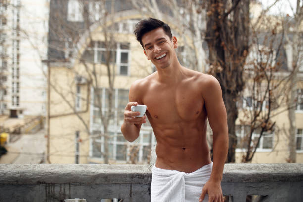 Smiling sexy man in bathroom towel on balcony have a breack coffe, posing outside. Horizontal view. stock photo