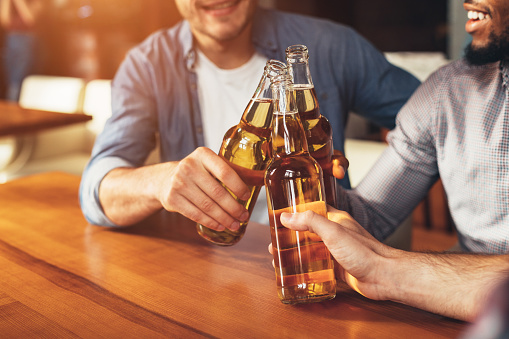 Friends clinking bottles of beer, resting together in bar