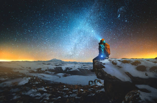 istock Night winter landscape a man with a backpack and a lantern on his head sits on a rock in the mountains 1150713046