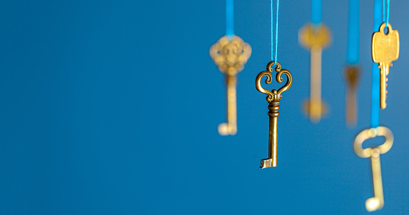 Many old keys of yellow gold color are hanging on thread on a blue background. The concept of the selection of access or password to the secret data. Copy space for text