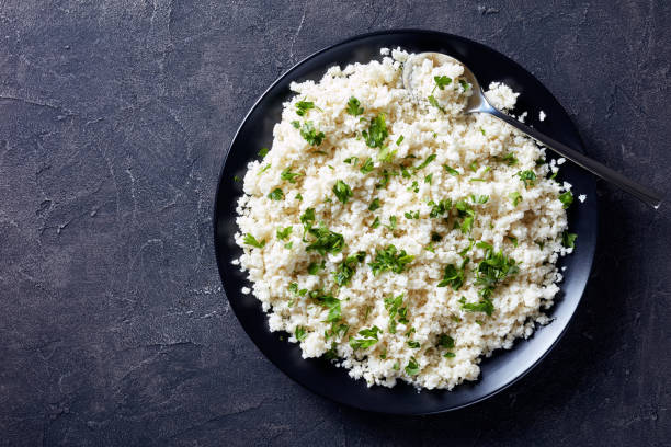 Cauliflower rice or couscous mixed with finely chopped parsley close-up of Cauliflower rice or couscous mixed with finely chopped parsley in a black bowl on a concrete table, horizontal view from above, flatlay finely stock pictures, royalty-free photos & images