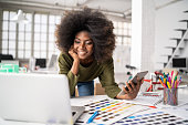 African Fashion designer working in studio and using laptop and smart phone