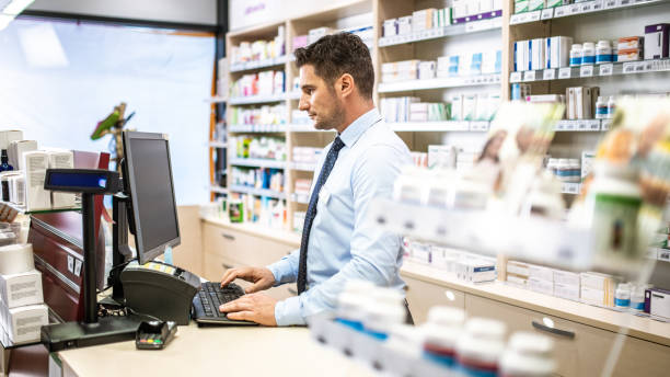pharmacien utilisant l’ordinateur dans la pharmacie - pill bottle pharmacy medicine shelf photos et images de collection
