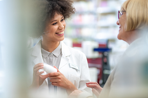 Pharmacist talking with senior female customer about medicine bottle in drugstore.