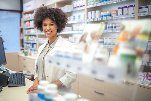 Portrait of smiling young pharmacist standing at counter in drugstore.