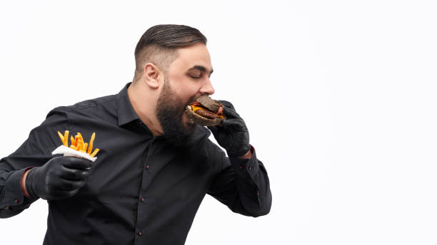 istock Man with french fries biting burger 1150718045
