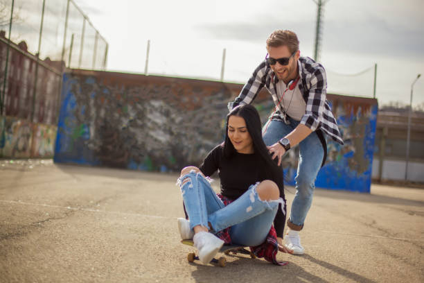 young couple having fun with a skateboard - pair couple mid adult happiness imagens e fotografias de stock