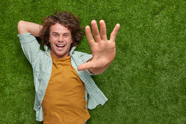 istock Man relaxing on grass and reaching out camera 1150723017