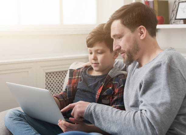 szczęśliwy ojciec i syn za pomocą laptopa w domu - wireless technology serious education enjoyment zdjęcia i obrazy z banku zdjęć