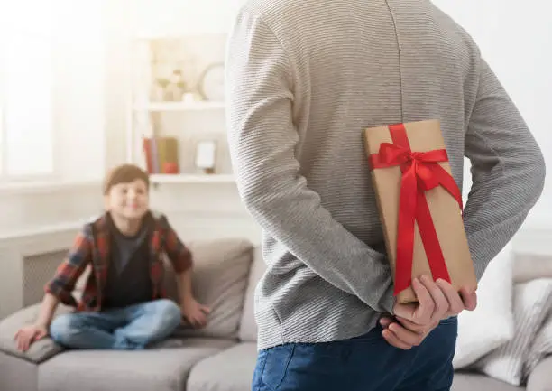 Father prepare gift case to impressed son sitting on sofa at home
