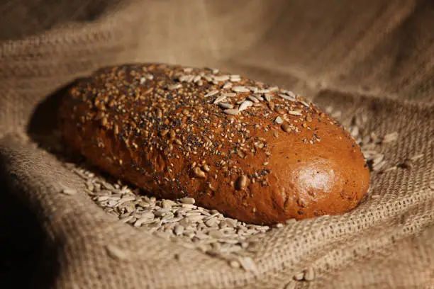 Loaf of grain bread lies on a jute sack in a pile of grains