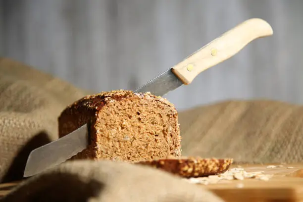 Sliced loaf of grain bread on jute bag, in which there is still a bread knife