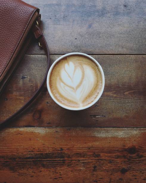 Overhead view of flat white coffee and handbag on a rustic wooden table