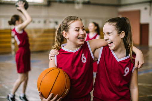 Cute teenage girls, smiling and embracing after basketball match, happy after winning the game leaving the sport field