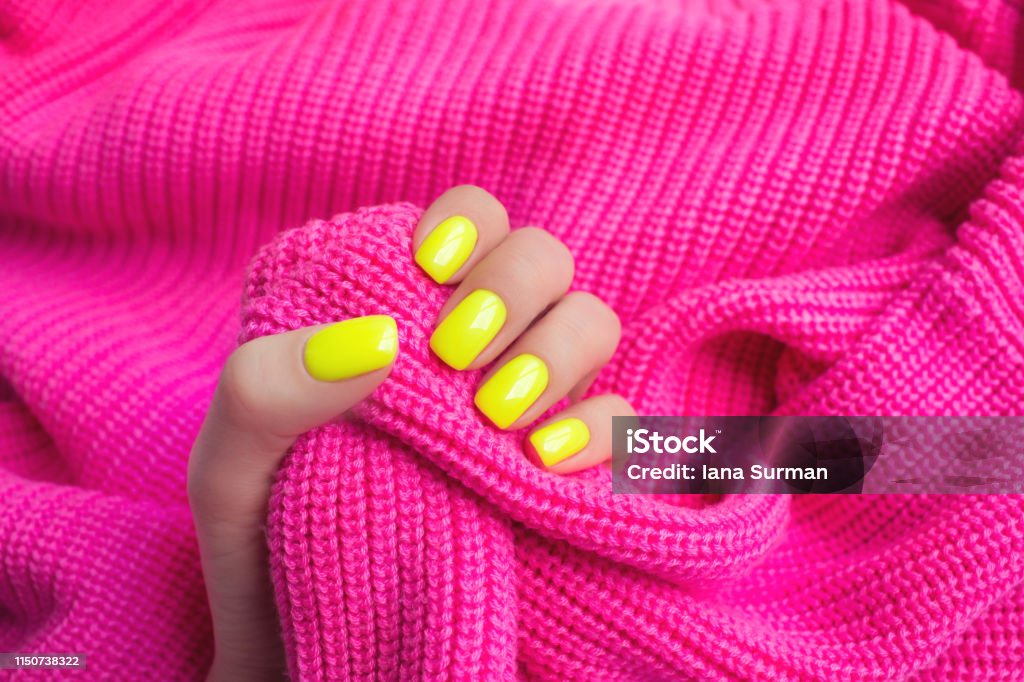 Stylish trendy female manicure. Neon yellow nails on plastic pink background. Nail polish. Art manicure. Modern style. Neon Colored Stock Photo