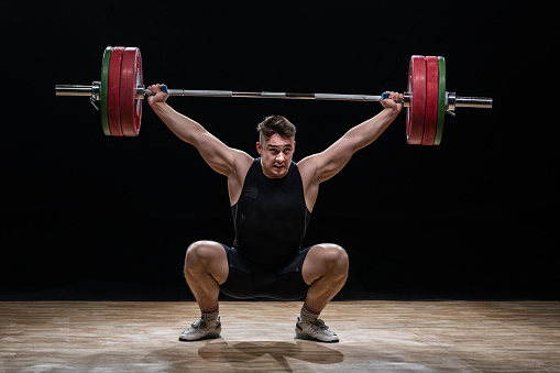Young man lifting barbell against black background.