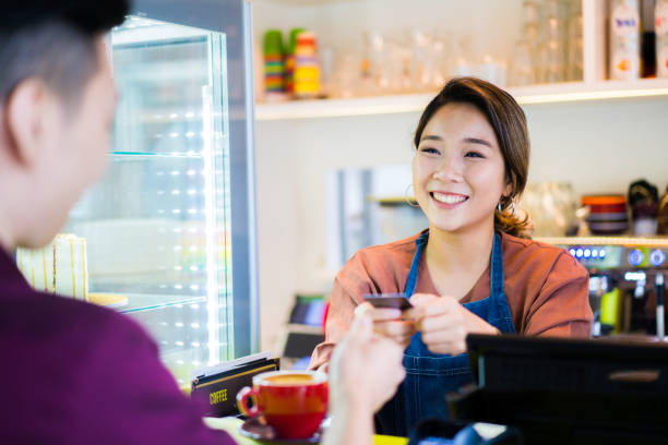 hermosa camarera asiática recibiendo pago con tarjeta de crédito del cliente en la cafetería. - delicatessen small business cafeteria bar counter fotografías e imágenes de stock
