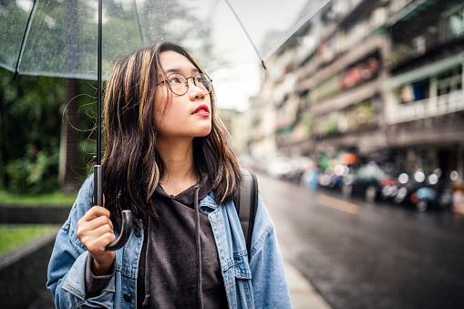 Asian girl walking in street with an umbrella.