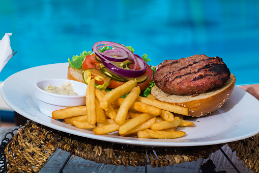 A plate with open hamburger and french fries, over a light blue swiming pool with all ingredients showing