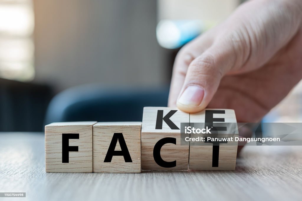 Business man hand holding wooden cube with flip over block FAKE to FACT word on table background. News, solution and business  concepts Artificial Stock Photo