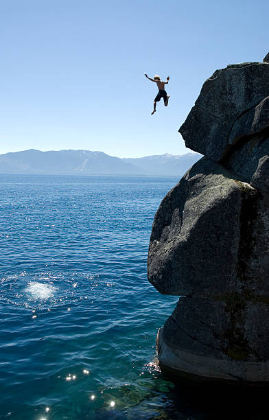 Man jumping off a cliff into the sea A young man leaps off a cliff at Lake Tahoe. A splash from an earlier jumper is seen below. Room for text on the right side shadow, or upper left sky. leap of faith stock pictures, royalty-free photos & images