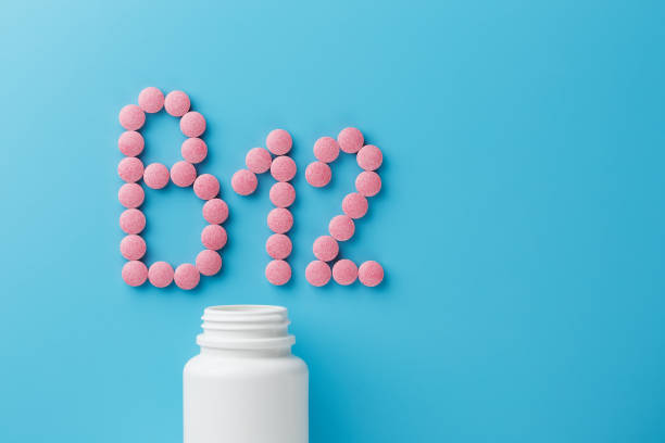 istock Pink round vitamins B12 shaped pills on a blue background spilled from a white can 1150760549