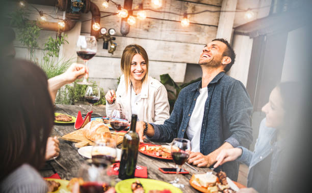 young friends having fun drinking red wine on balcony at house dinner party - happy people eating bbq food at fancy alternative restaurant together - dining lifestyle concept on desaturated filter - wine dinner party drinking toast imagens e fotografias de stock