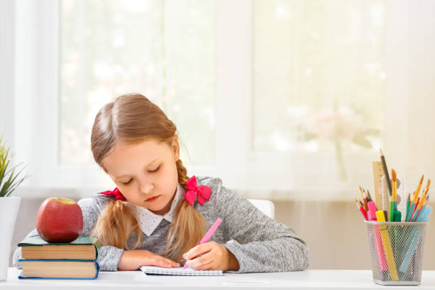 istock A little girl student sits at the table and writes in a notebook on a blurred background. The concept of education and school. 1150766620
