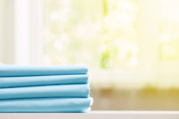 istock Close-up of blue clean bedding on a blurred background. A stack of folded bed sheets on the table. Sunlight from the window. 1150767182