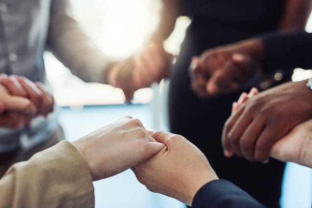 We're all here to help each other succeed Cropped shot of a group of businesspeople standing together and holding hands in a modern office praying photos stock pictures, royalty-free photos & images