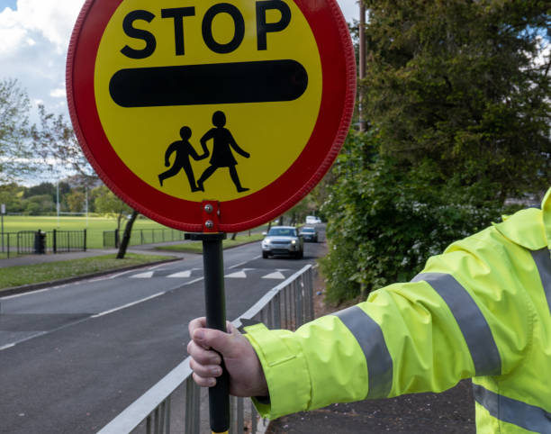 A school crossing guard preparing to stop traffic The arm of a crossing guard, known as a lollipop man or lady in the UK, preparing to stop traffic so school children can cross the road safely. He stands close to the school gates when the area is busy with children going to and from school. He is wearing bright reflective clothing so he can be seen clearly by oncoming drivers. When the road is safe and traffic has stopped children are guided across the road safely. hazard sign photos stock pictures, royalty-free photos & images